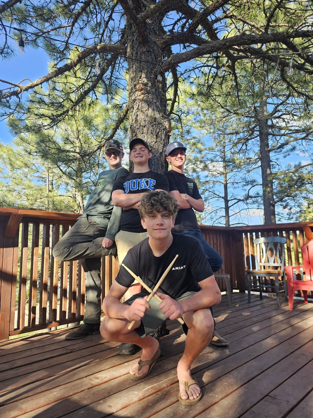 The four members of Dueling Durkins Band posing on a wooden deck under tall pines